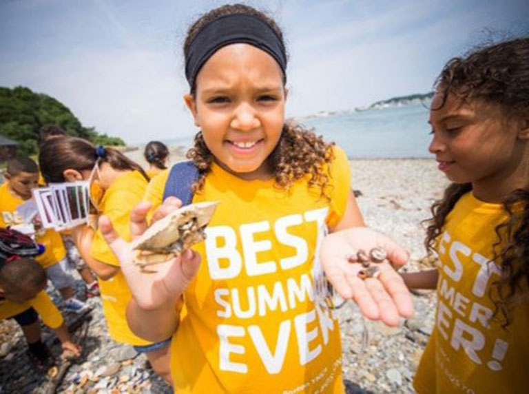 Student holding crab shell and sea shells found on beach