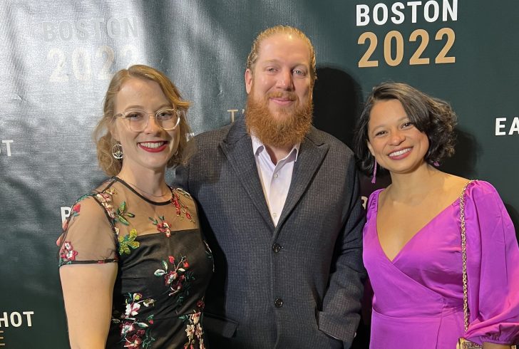 Two women and a man in formal wear standing together in front of a backdrop that says "Earthshot Boston 2022."