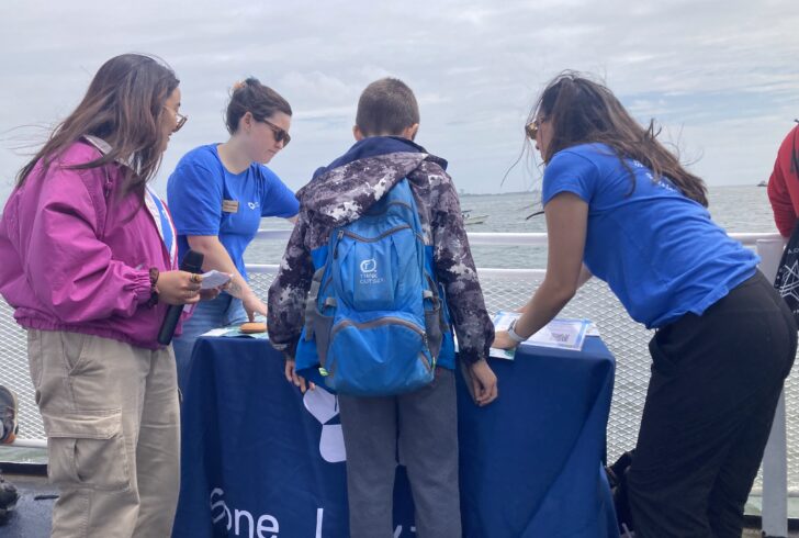 SLL Educators, Jasmine Perez, Liana Greenberg-Nielsen, and Daria Healey showcasing a map of the Boston Harbor Islands to an interested youth participant.