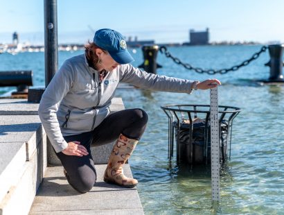 A woman kneeling on granite steps, holding a meter stick in the surrounding floodwaters.