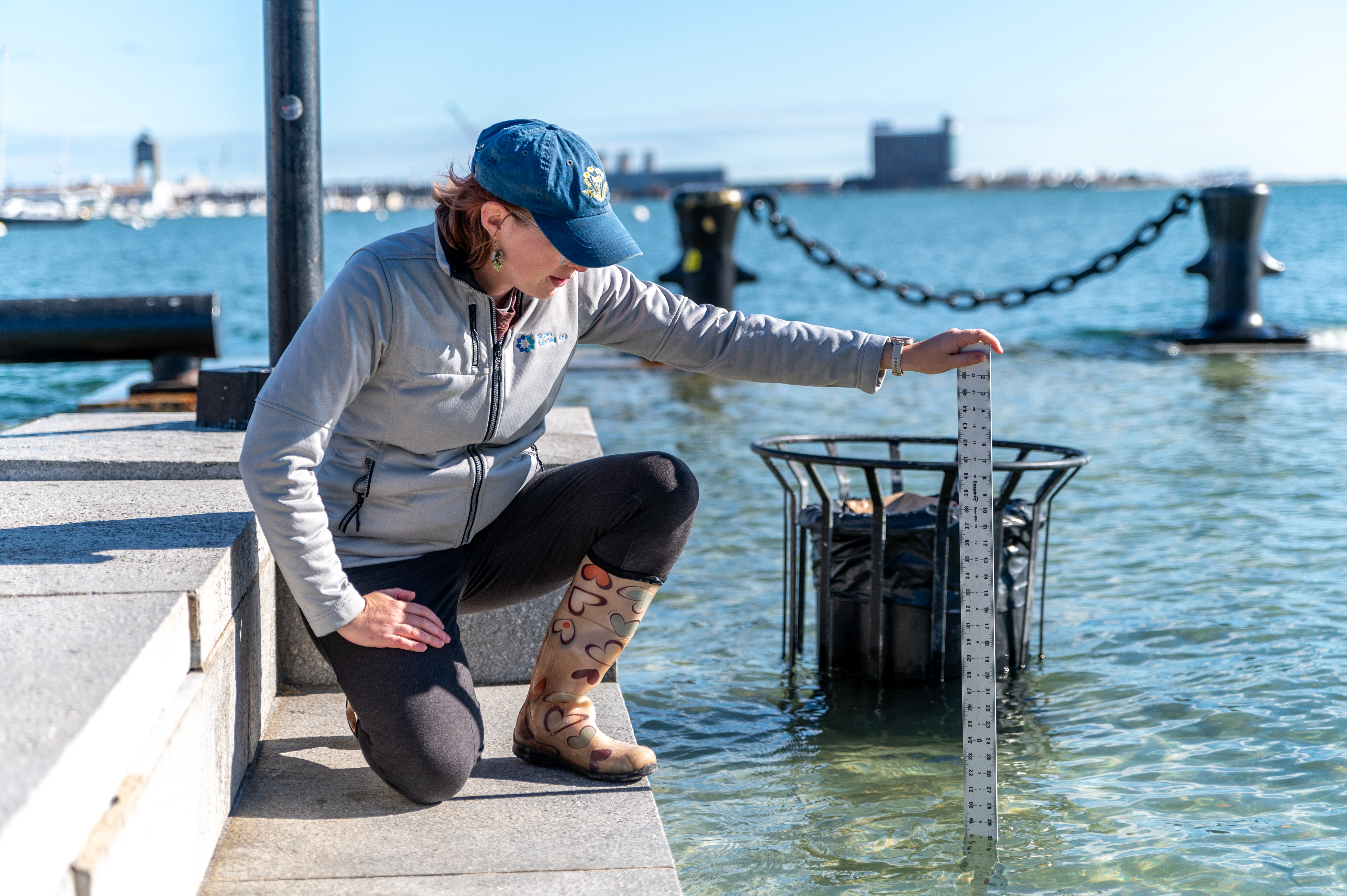 A woman kneeling on granite steps, holding a meter stick in the surrounding floodwaters.